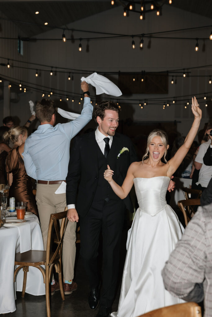 Bride and groom | celebrating and walking into reception with raised arms | wedding reception dance floor